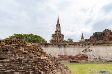 Fototapeta premium Ancient stupa and temple ruins behind a weathered brick wall at Wat Phra Ram in Ayutthaya, Thailand