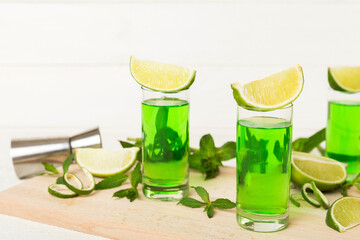 Sweet refreshing mint liqueur, with ice and mint leaves on table background, Shots with lime slice and mint flat lay