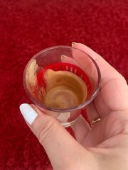 Woman holding an empty cup of espresso coffee against a red background 