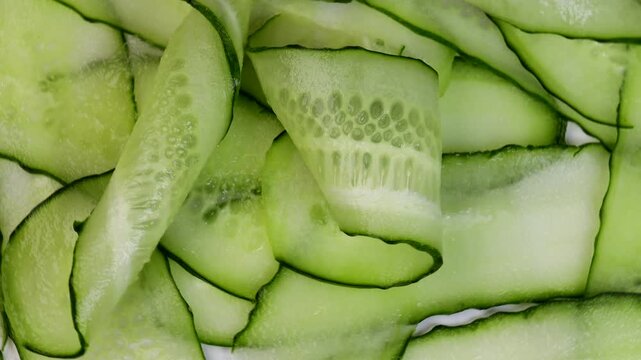 rotating thin cucumber slices in circular motion. macro video of raw green vegetable with visible texture and peel. concept of healthy eating, vegetarian cooking, food preparation