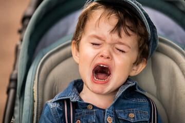Little boy in denim cap crying outside