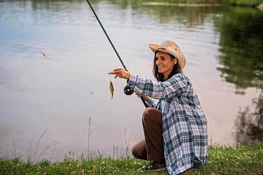 woman is fishing in a lake holding a small fish on a hook.