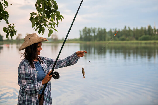 woman is fishing in a lake holding a small fish on a hook.
