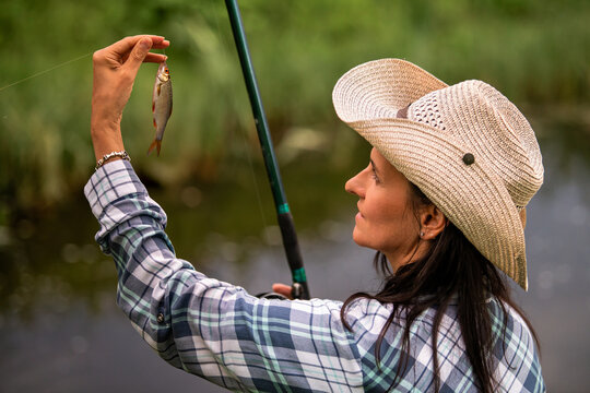 woman is fishing in a lake holding a small fish on a hook.
