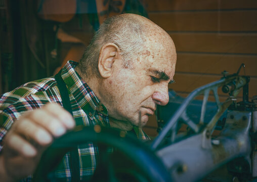 Elderly shoemaker turning handwheel of vintage sewing machine