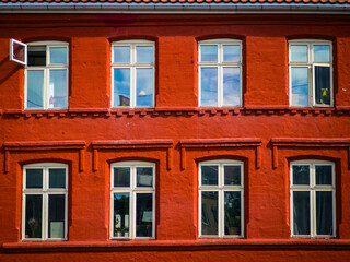 Fototapeta premium Vibrant Red Brick Building Facade with Symmetrical White Windows in Urban Setting Capturing Reflective Sky