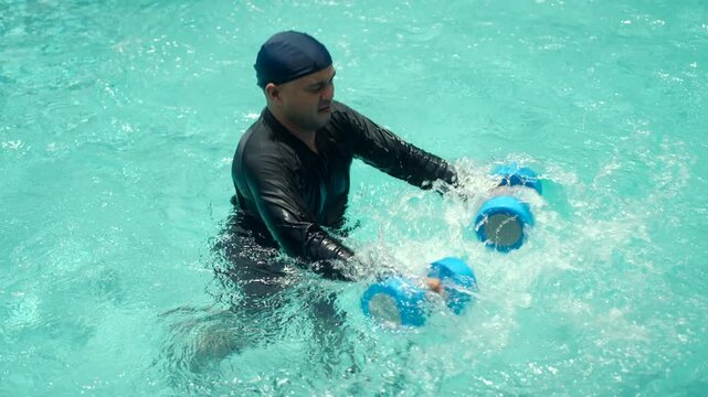 Man in a swim cap and rash guard relaxes and exercises in the pool, holding blue aquatic dumbbells, highlighting hydrotherapy, water fitness, and refreshing aquatic workouts.