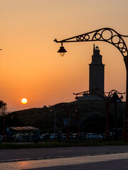 Silhouette of historic lighthouse framed by ornate street lamps at sunset