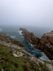 Misty rugged coastal cliffs and jagged rocks jutting into stormy sea