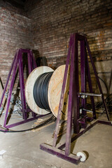 Large wooden reel with black cable on a purple metal stand in an old brick building. Electrical...