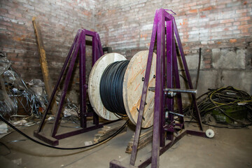 Large wooden reel with black electrical cable on a purple metal stand. Industrial wire spool for...