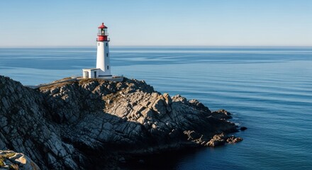 Rocky coastline with white lighthouse facing calm, blue ocean on a sunny day