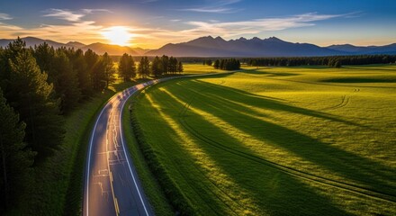 Scenic road curves through green fields at sunset, mountains in distance