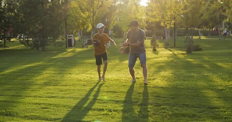 Father and son play rugby in park at sunset. Man, child run and throw ball with joy, enjoying outdoor sport and bonding. Happy dad son share active moment in nature. Sports family scene in golden hour - Powered by Adobe