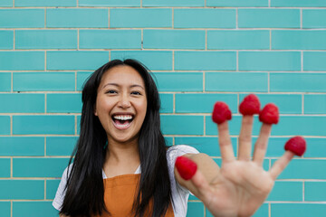 Smiling grocer displaying raspberries on fingers in shop