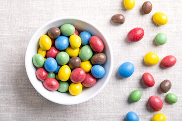 Candy coated milk chocolate peanuts, in a white bowl, on linen fabric. Roasted peanuts, coated with milk chocolate, coated with sugar and not so color-intensive organic colors. Close-up from above.