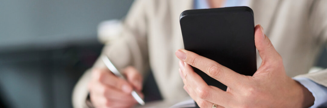 Businesswoman working at office using smartphone and writing notes