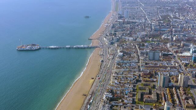 4K drone panorama of Brighton seafront : Palace Pier juts into the English Channel, sandy beach and busy promenade meet the city grid, with the Brighton i360 tower on the horizon.