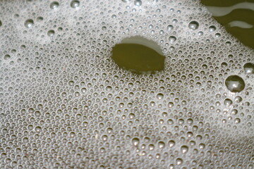 Close-up of white foam and bubbles floating on the surface of murky green water, creating a textured pattern.