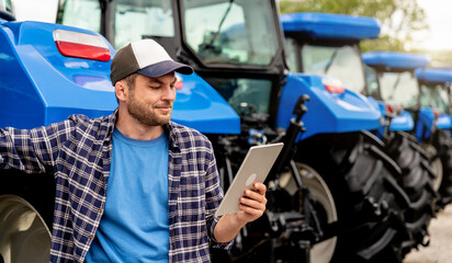Smiling man in casual clothes using digital tablet near tractors at agricultural dealership © Igor Barilo