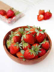 a bunch of ripe strawberries in a wooden bowl on white background