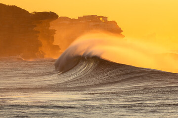 Powerful waves crash at Bronte Beach, Sydney, captured during golden light as sea spray dances in...