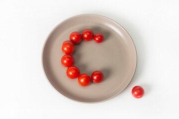 A group of cherry tomatoes lie on a grey plate in the shape of the letter C. Tomatoes contain a lot of vitamin C