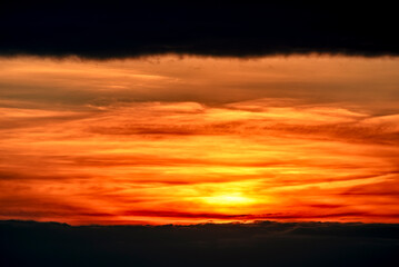 Die von Wolkenschleihern verdeckte, unter- oder aufgehende Sonne scheint durch ein sich in der...