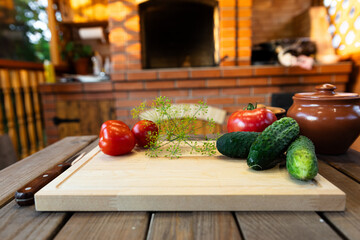 Cutting board on a wooden table, surrounded by fresh vegetables like tomatoes and cucumbers. Rustic...