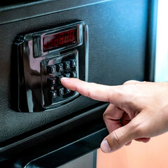 Hand try to press button on modern keypad lock on safe at home decor store. Customer choosing security cabinet with digital display for valuables storage. Entering password number to unlock secure box