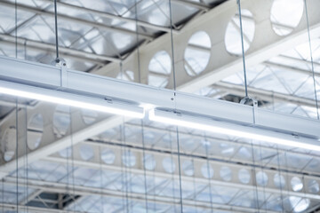 Long light lamp hanging on the ceiling under the cellular beam and steel truss. Industrial building construction site. Warehouse or factory roof structure and lighting design