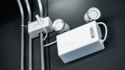 LED Automatic emergency light mounted on black wall in industrial warehouse or factory building. Backup on battery when power outage