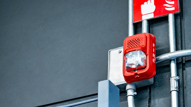 Fire alarm siren with flashing strobe light and symbol sign on the wall in industrial warehouse or factory building. Emergency fire warning system equipment