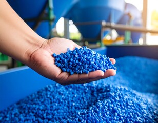 Handful of blue plastic resin pellets against a backdrop of a larger quantity