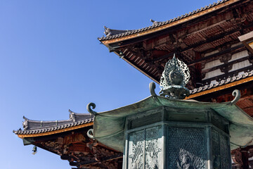 Detailed bronze lantern and traditional tiled wooden eaves of Todai-ji Temple in Nara Japan captured against bright clear sky on sunny day