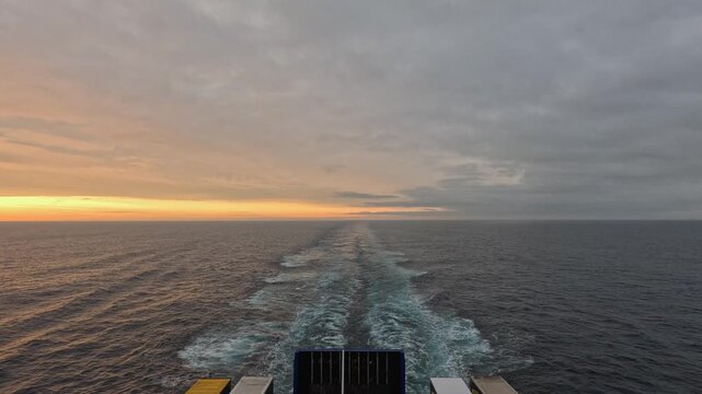 Wake of transport ferry sailing on grey overcast day, golden horizon