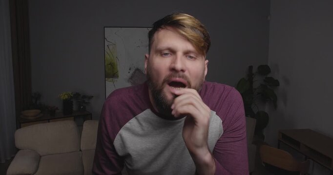 Close up blonde bearded European  man looking to camera or out a window and clutching his head in horror and shock, it's hard to breathe, panic attack, biting nails and fingers