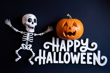 Fototapeta premium Playful Halloween Composition Skeleton with Raised Arms Beside a Carved Pumpkin and 'Happy Halloween' Text on a Dark Background
