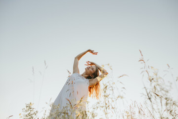 Woman dancing in nature wearing white dress at sunset