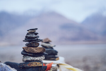 Colorful stacked stones near traditional prayer flags with soft Himalayan mountain background in Ladakh for spiritual balance