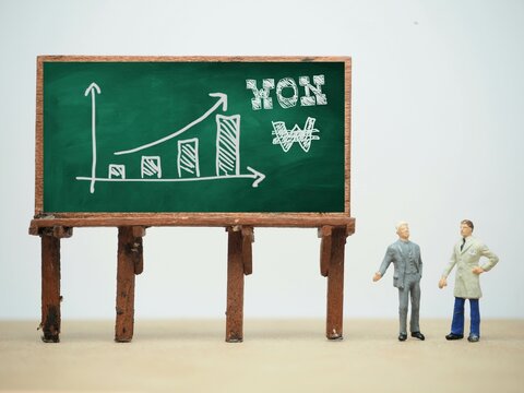 Mini toy of action figure at table with blurred background. Business financial photography concept design. Minifigure of businessman character with South Korea Won graph at board Raise up chart arrow