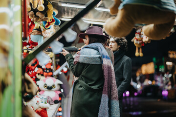 A man and woman participate in a carnival shooting game surrounded by stuffed toys, expressing engagement and enjoyment during an evening winter fair experience.