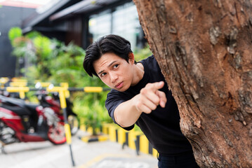 Suspicious young man animatedly pointing while secretly spying on ex-boyfriend talking to someone...