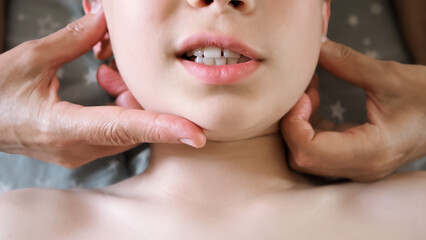 The masseur is massaging child's face. A session of therapeutic lymphatic drainage massage. Physiotherapy treatment. An osteopath removes tension from the jaw muscle and relieves pain in a joint.