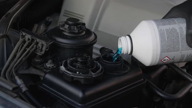  Male hands in gloves opening the cap and pouring blue liquid from a canister into a tank in a car. Taking care of the engine compartment, slow motion 200 fps