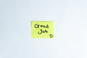 Yellow sticky note with handwritten “good job” and a smiley face at the bottom, attached to a clean white wall. Perfect for motivation, appreciation, and positive office or school messages.