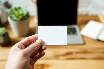 Obraz premium Hand holding blank business card mockup in cozy workspace with notebook. White card template against marble table background. Perfect for branding presentation.