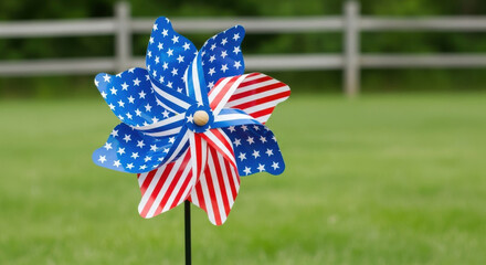 Patriotic american flag themed pinwheel spinning in a green grassy field with a wooden fence