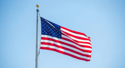 Obraz premium American flag waving proudly against a clear blue sky on a sunny day