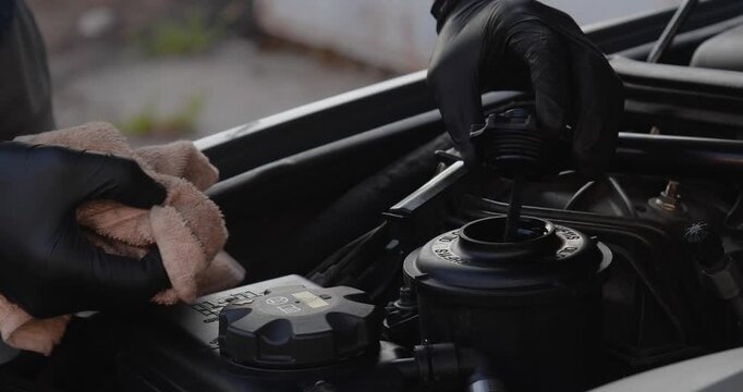  Male hands in gloves check the oil level with a dipstick in a car. Taking care of the engine compartment